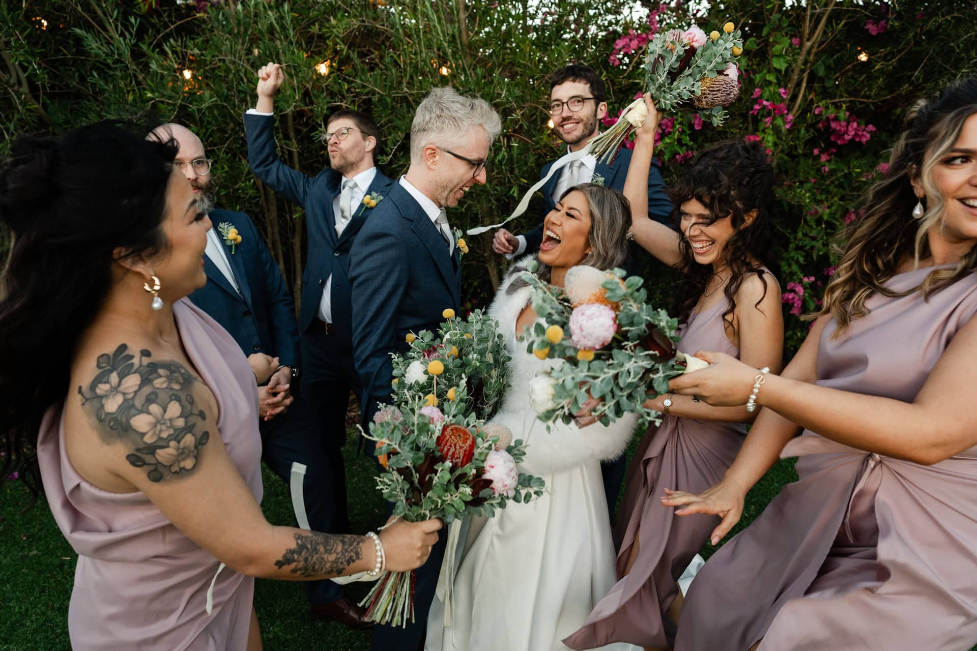 Perth wedding photographer wedding party wearing blue suits and lavender dresses dancing and laughing in a circle at Fremantle wedding