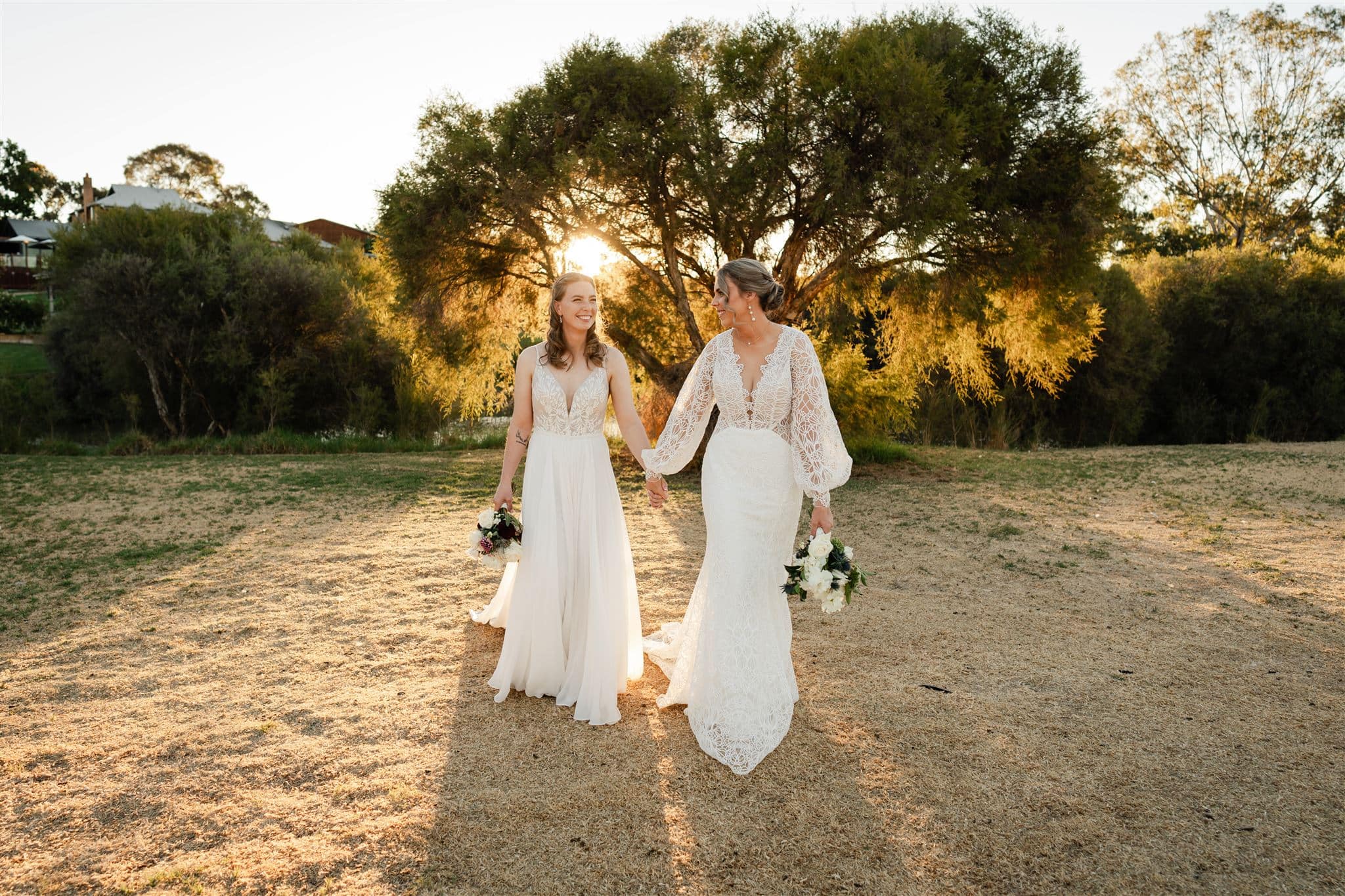 Perth wedding photographer two brides wearing white dresses walking holding hands with warm sunset golden light at Perth wedding