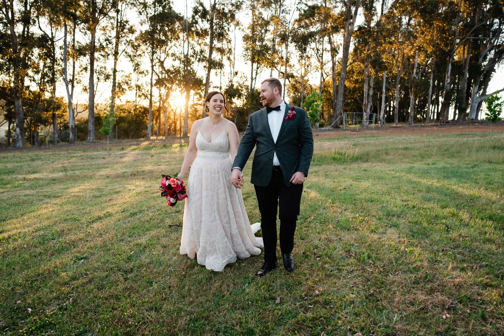 bride wearing white dress and groom wearing suit with green jacket holding hands walking at sunset at Perth wedding