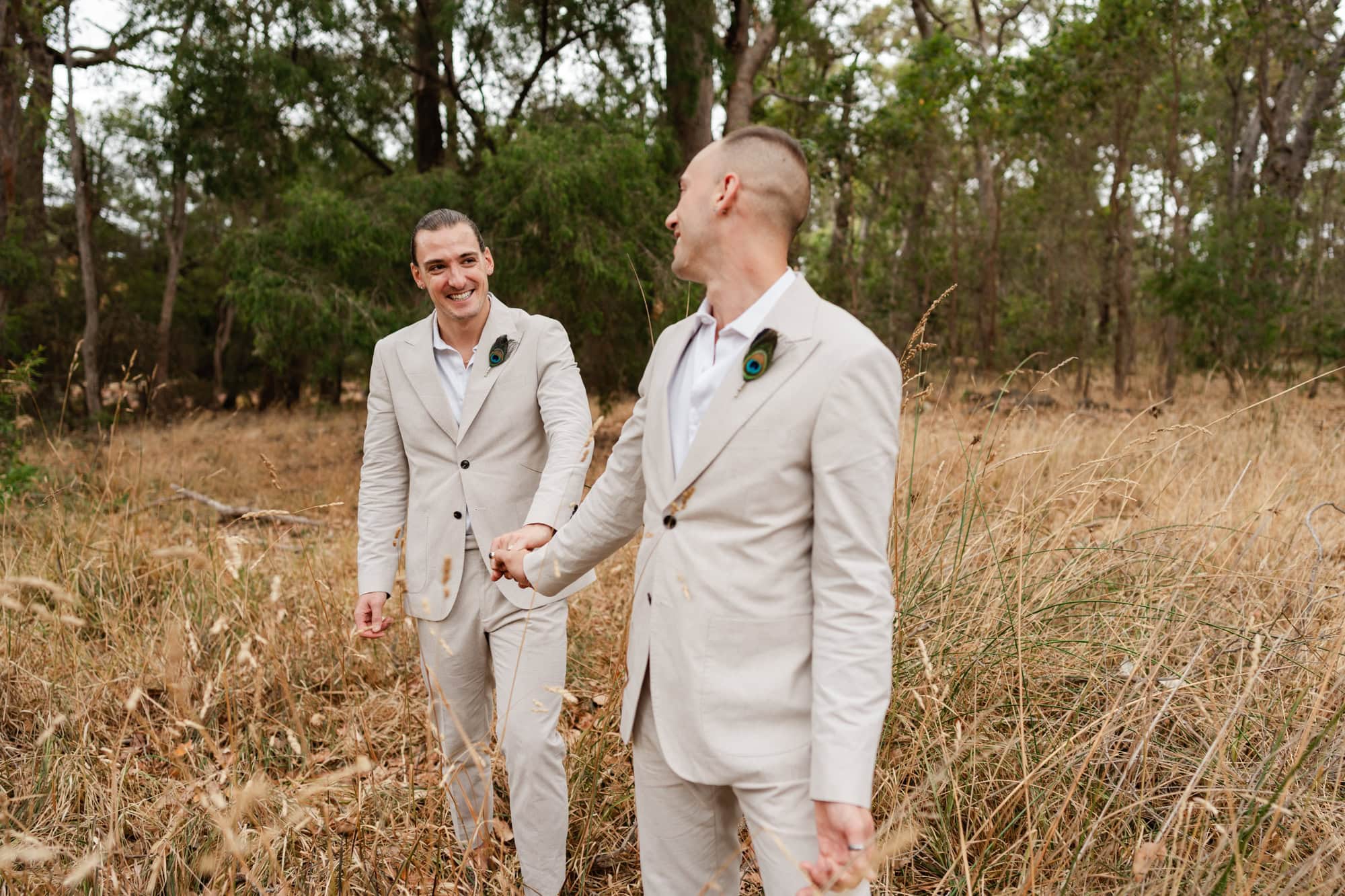 wedding photos Perth two grooms wearing cream coloured suits walking holding hands in field