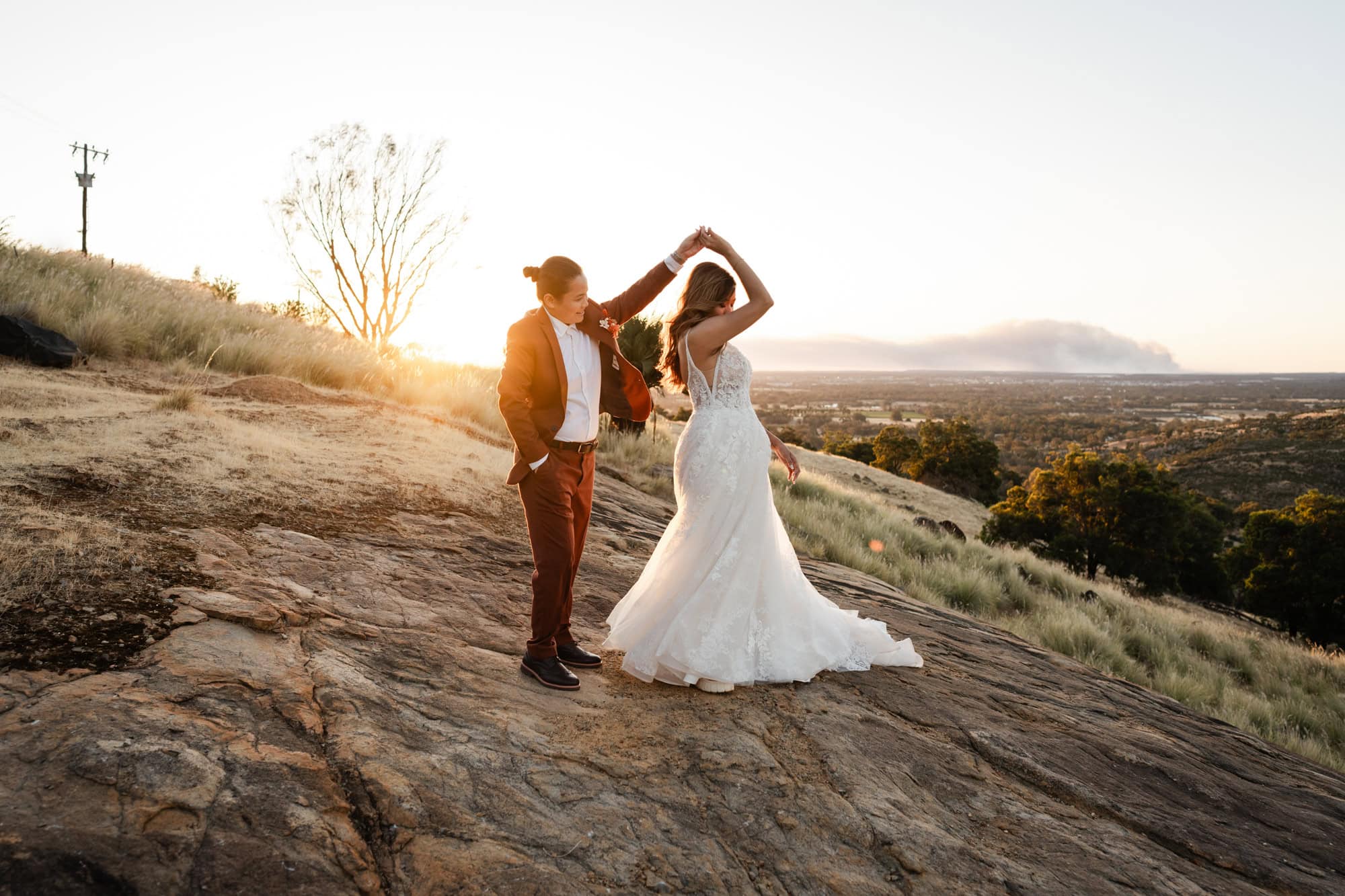 wedding photos Perth bride wearing maroon suit twirling bride wearing white dress on rock at sunset