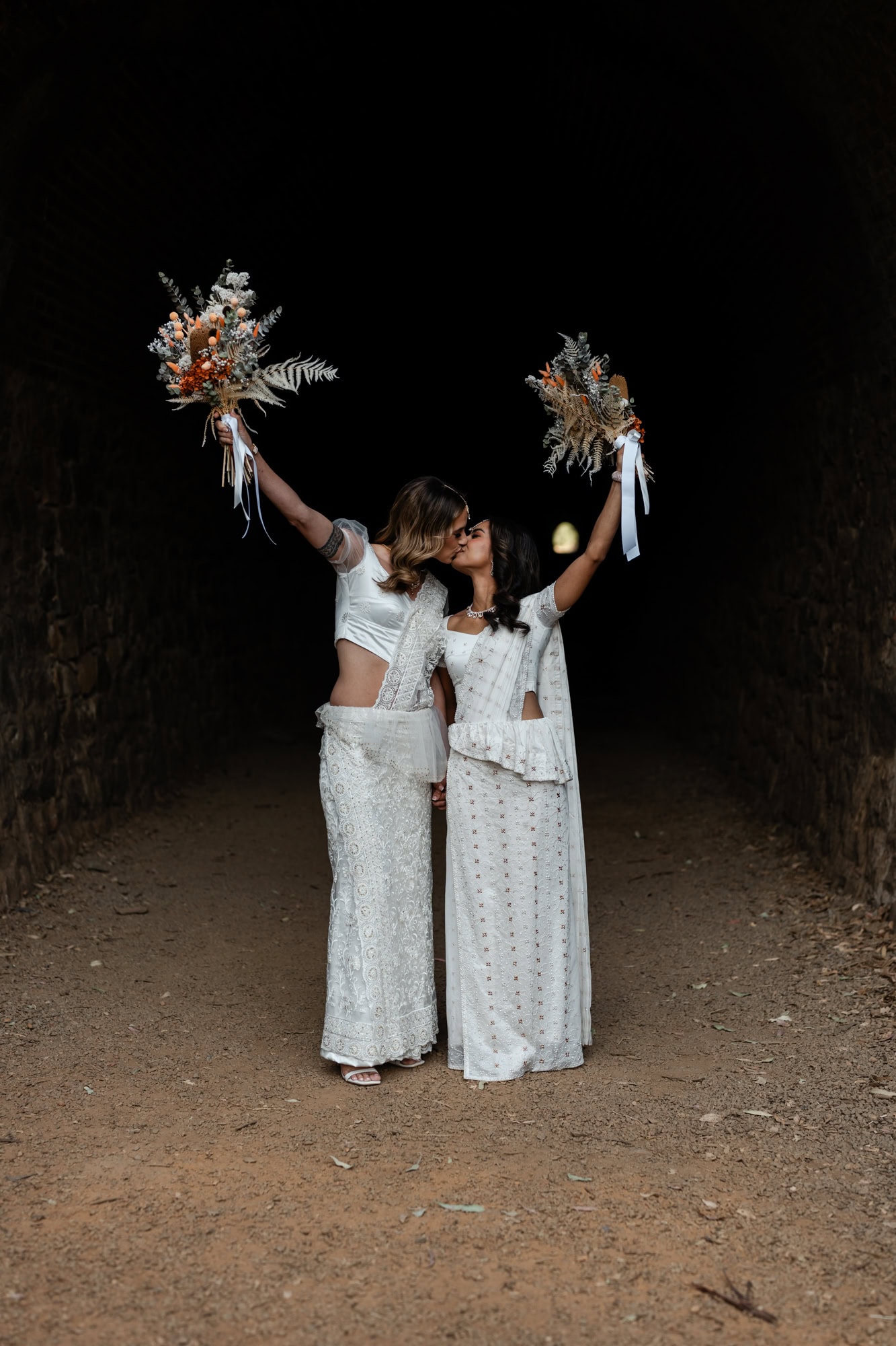 wedding photos Perth two brides wearing white sarees kissing holding bouquet in air