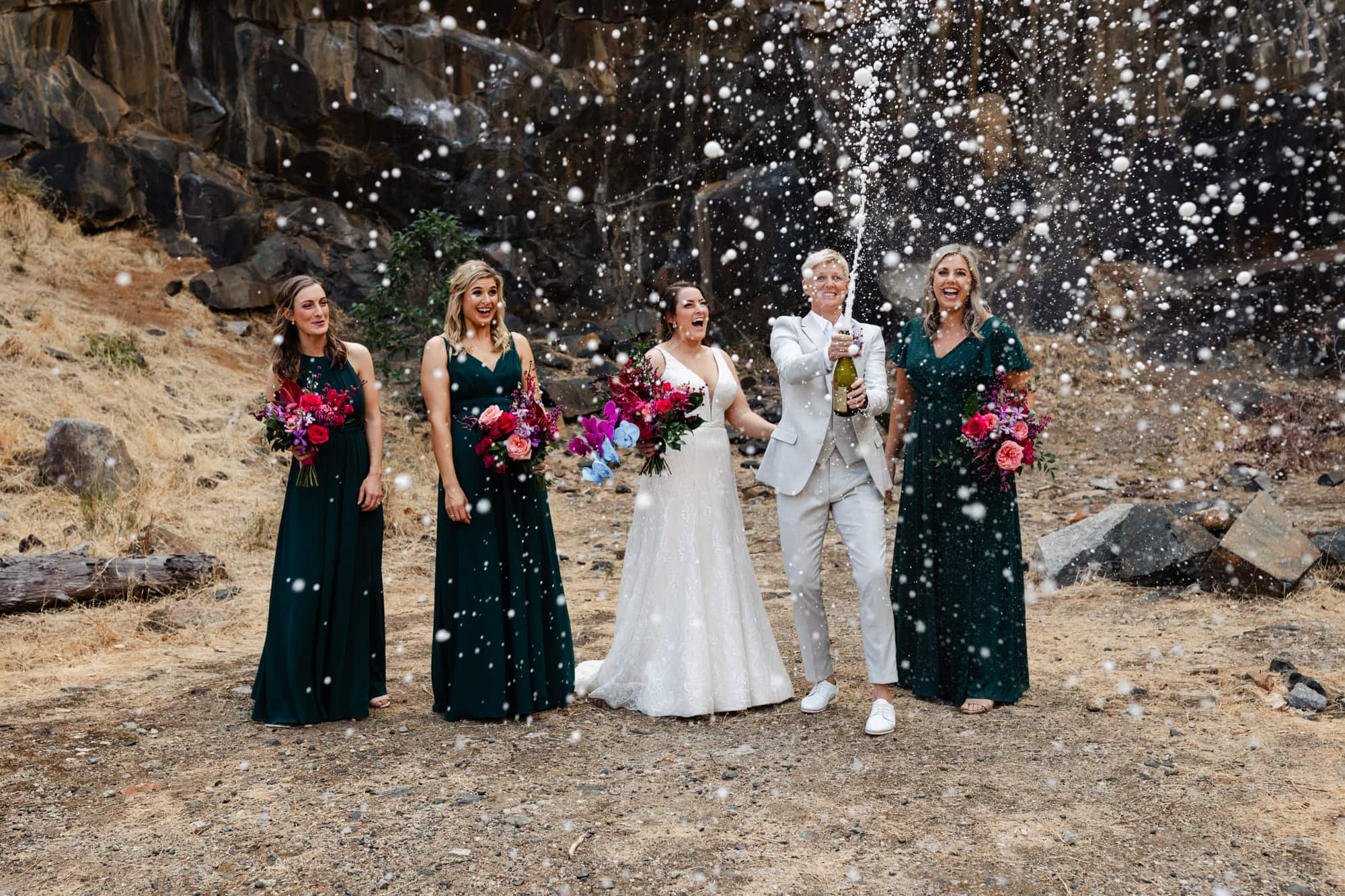 wedding photos Perth bride wearing cream suit spraying champagne with bride wearing white dress and bridesmaids wearing green dresses