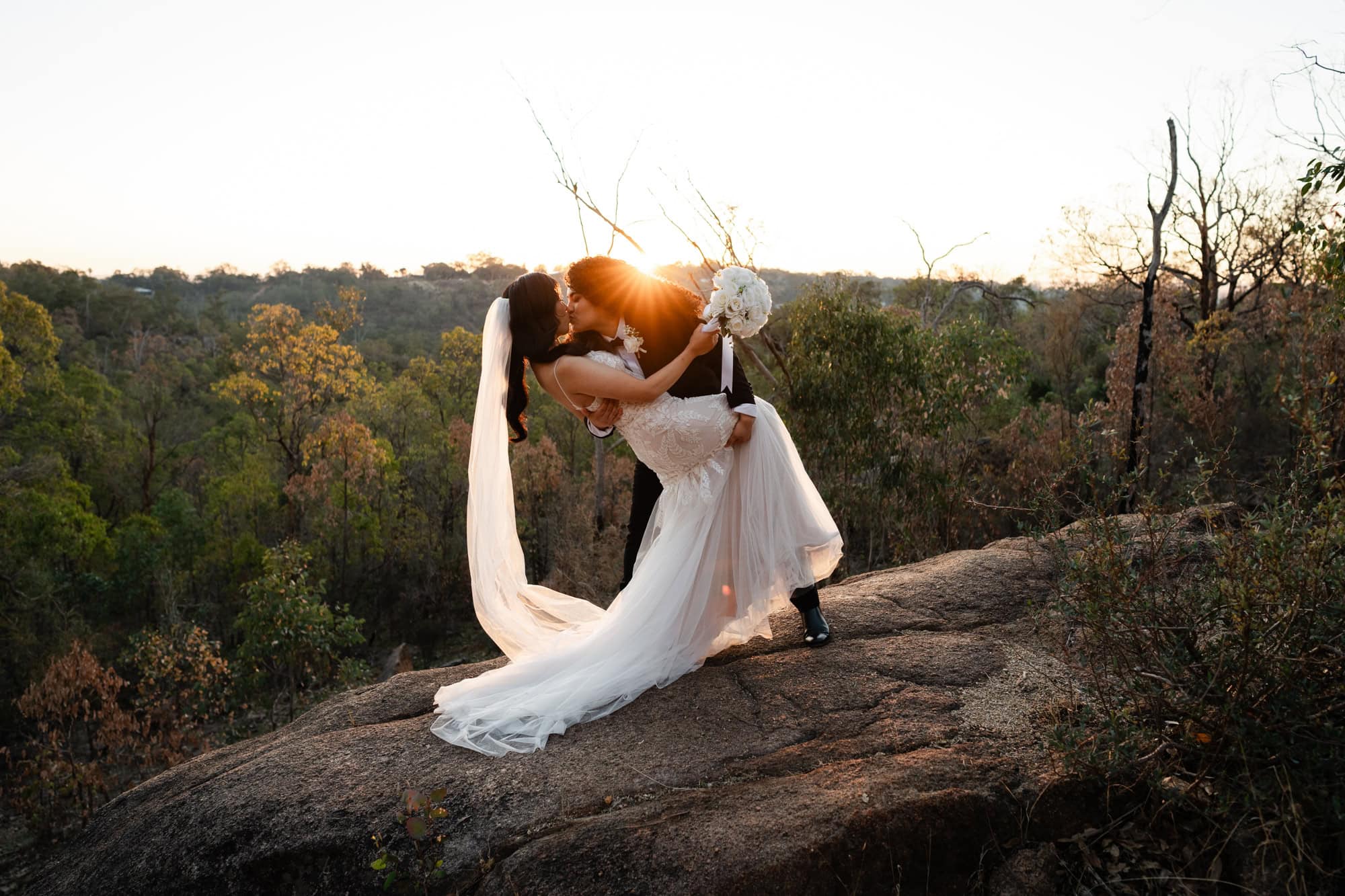 wedding photos perth bride wearing black suit dipping and kissing bride wearing white dress on cliff at sunset