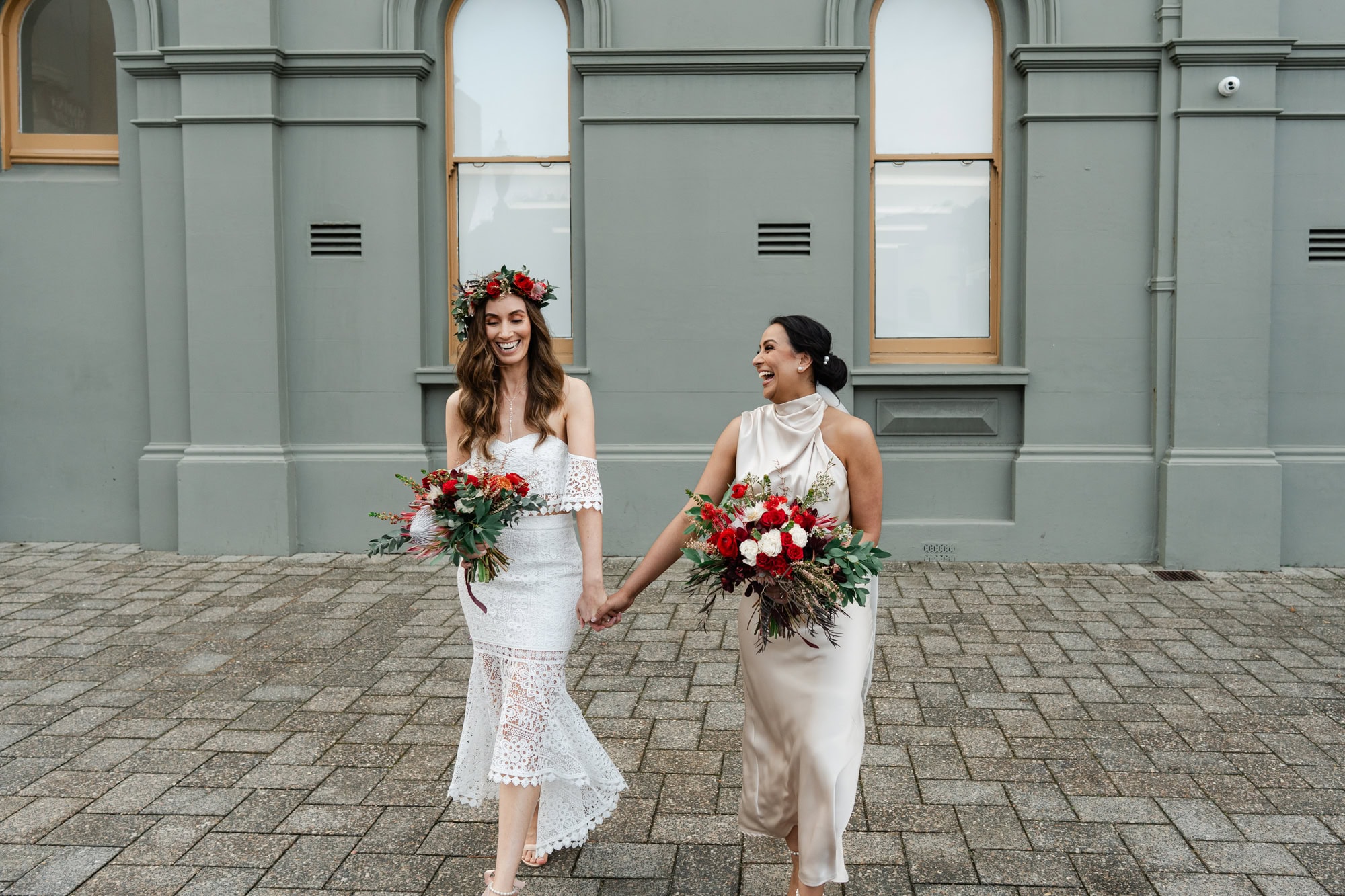 wedding photos Perth two brides holding hands and carrying red white bouquets laughing