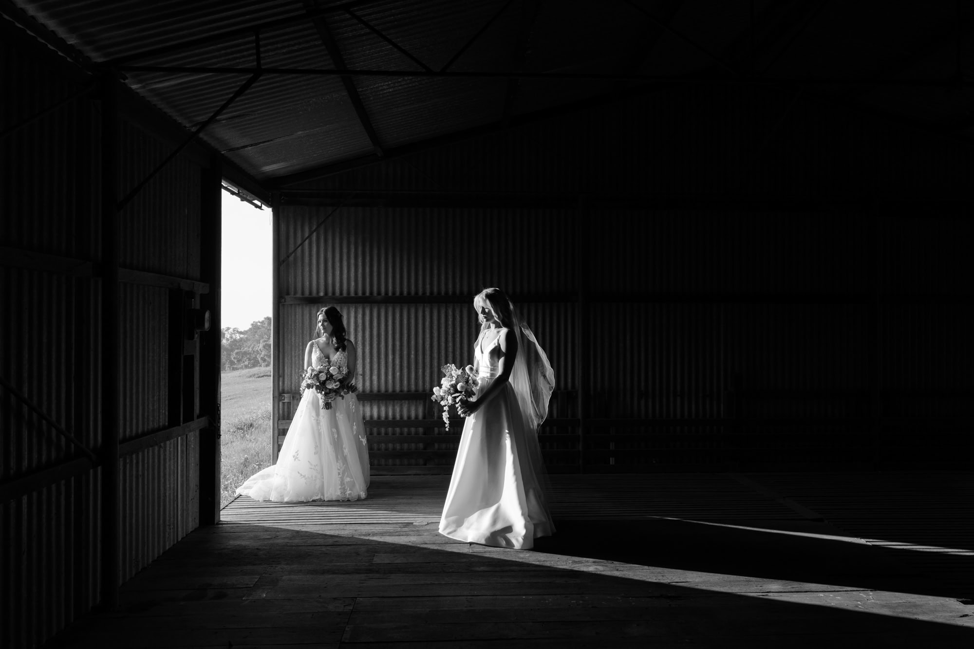 wedding photos perth two brides standing in dark shed apart with light streaming in