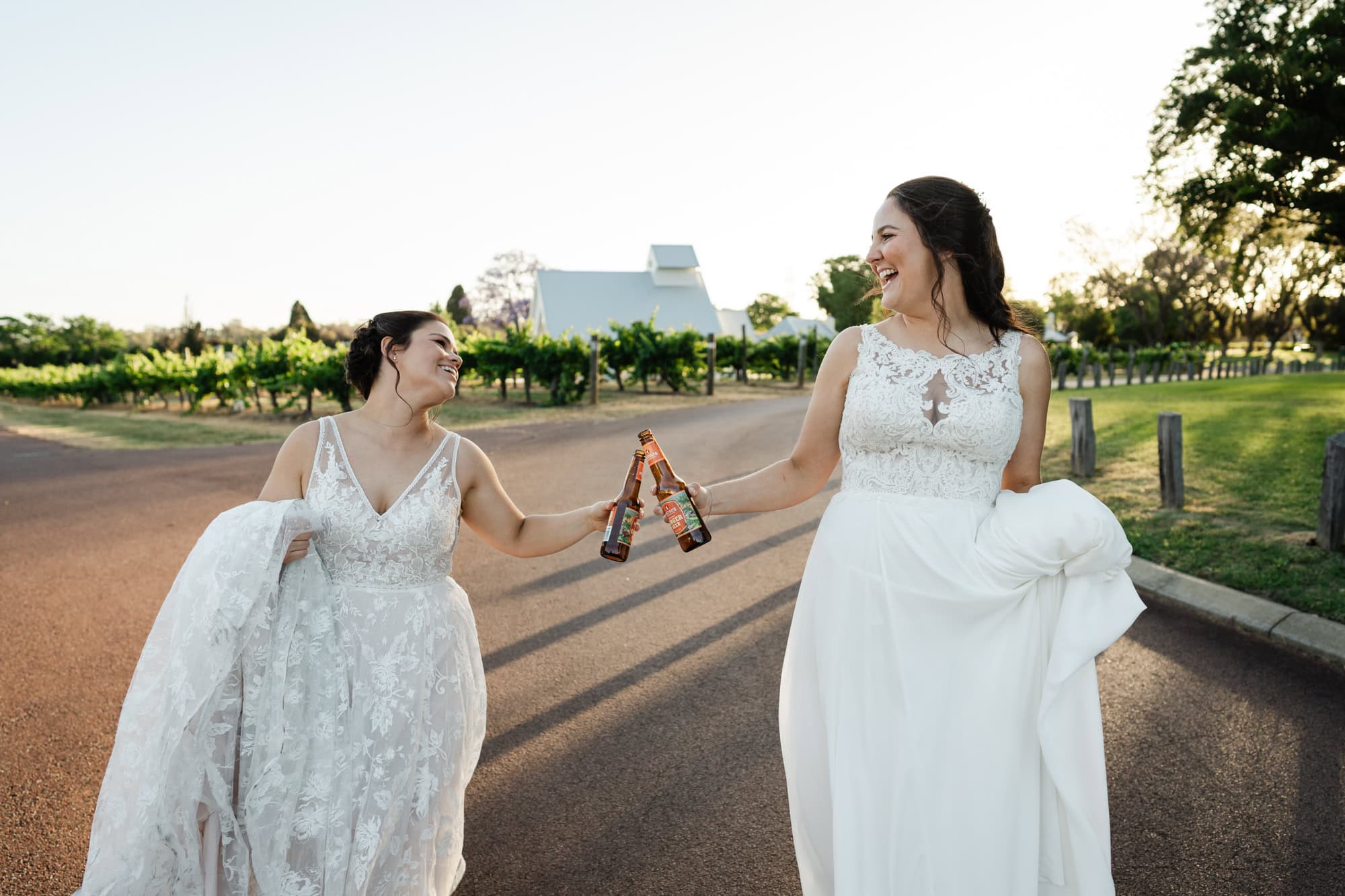 wedding photos Perth two brides wearing white dresses holding beer walking laughing