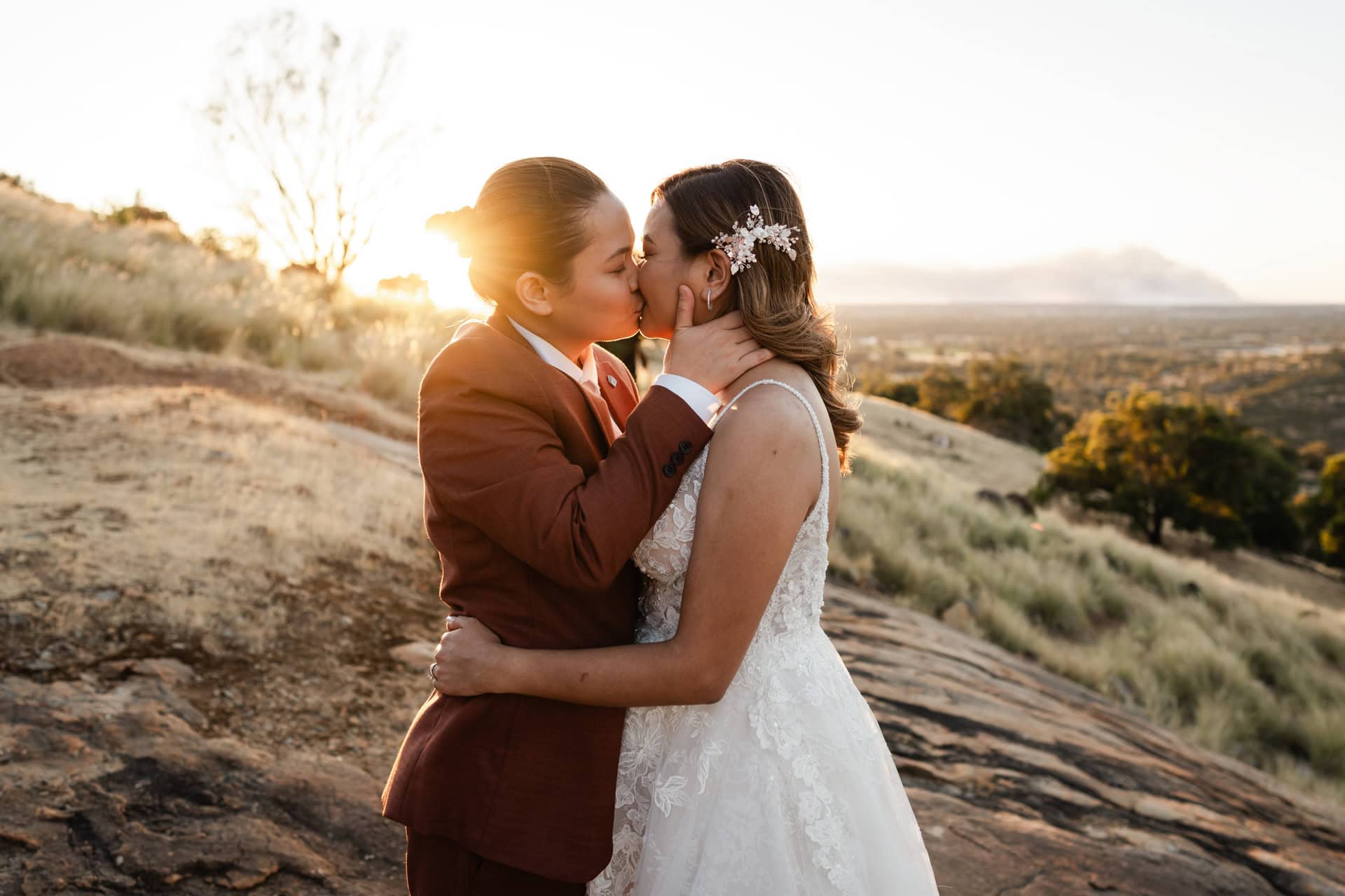 wedding photos perth bride wearing maroon suit kissing bride wearing white dress at sunset